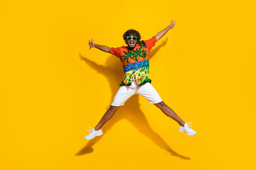 Full length photo of eccentric guy wear hawaii shirt sneakers in glasses raising arms up jumping isolated on yellow color background - obrazy, fototapety, plakaty