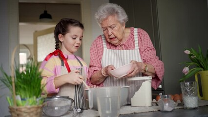 Grandmother with grandaughter preparing traditional easter meals, baking cakes and sweets. Passing down family recipes, custom and stories.