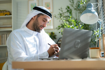 Portrait of young Arabic businessman working on laptop at home