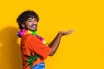 Side profile photo of funky man dressed print shirt flower necklace arms present product empty space isolated on yellow color background