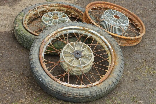 three old rusty dirty discarded wheels with spokes with rubber black tires from a motorcycle lie on the ground during the day on the street