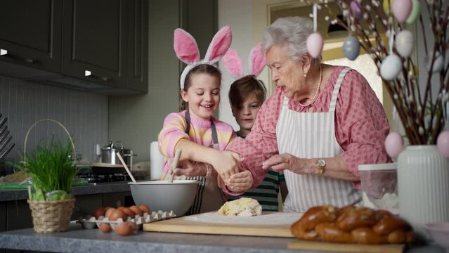 Grandmother with grandchildren preparing traditional easter meals, kneading dough for easter cross buns. Passing down family recipes, custom and stories.