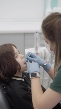 A pediatric dentist applies fluoride varnish to a child's teeth with a brush. Regular fluoridation to prevent caries and maintain oral health. The patient is in the dentist's office.