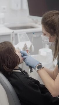A pediatric dentist performs fluoridation of a child's baby teeth. The use of fluoride for the prevention of caries and maintenance of oral hygiene. The patient is in the dentist's office.