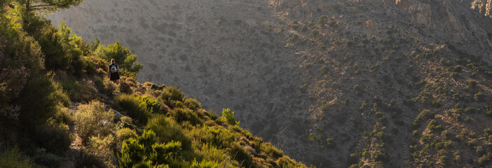Back view of a backpacker girl hiking on a mountain trail in the lush Halari canyon on the mountainuous North Aegean Island of Ikaria.	