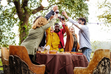 Diverse friends toasting at party - multicultural young people clinking wine glasses - joyful outdoor gathering