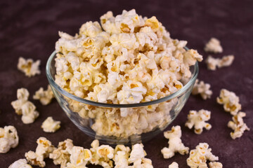 Popcorn in a glass transparent bowl on a dark background.
