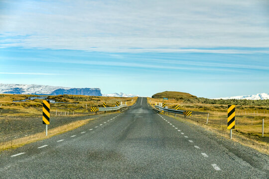 Straight road over a narrow bridge through barren terrain in Iceland.