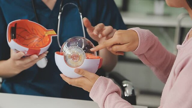close up of asian female doctor wearing face mask is showing eyeball model and explaining about eyes disease to elder senior man patient in hospital