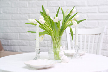 Beautiful table serving for Easter celebration in dining room, plates, bunny, vase with flowers. Easter table setting.