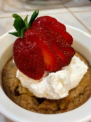 Delicious deep dish chocolate chip cookie with homemade whipped cream and fresh sliced strawberry on top