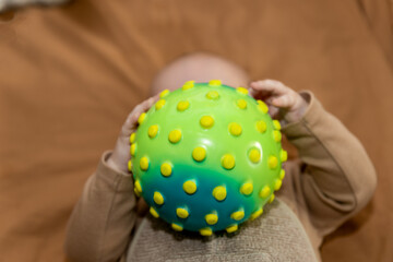 Dziecko, trzymające piłkę sensoryczną, aktywnie uczące się dotyku i chwytu, reprezentuje koncepcję edukacyjną i rozwoju malucha. koncepcja rozwijania zmysłów i umiejętności motorycznych po przez zabaw - obrazy, fototapety, plakaty