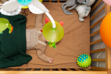 Dziecko leżące w łóżeczku podczas zasypiania, skupione na oglądaniu karuzeli z zabawkami, w tym małą piłką, ilustruje koncepcję rodzicielskiej opieki i pielęgnowania.