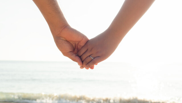 Summer time image of a couple holding hands. The groom with the bride in his arms. and diamond engagement ring on her finger.