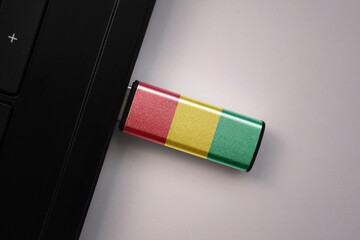 usb flash drive in notebook computer with the national flag of guinea on gray background.
