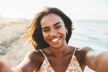 Beautiful black young woman taking selfie picture walking on the beach - Delightful female smiling...
