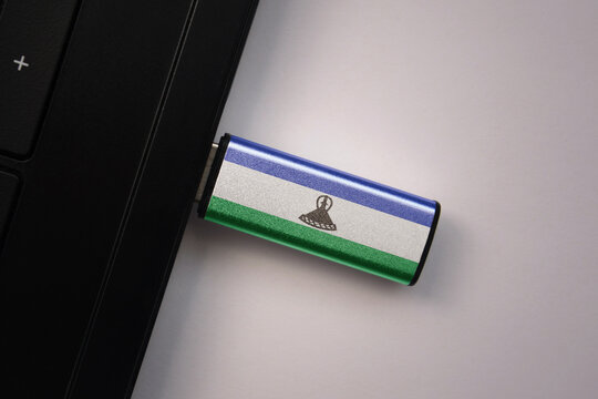 usb flash drive in notebook computer with the national flag of lesotho on gray background.