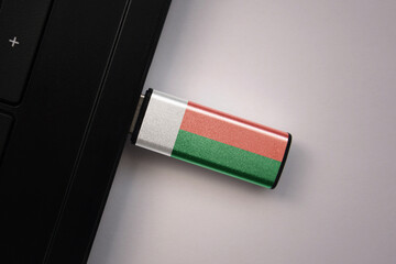 usb flash drive in notebook computer with the national flag of madagascar on gray background.
