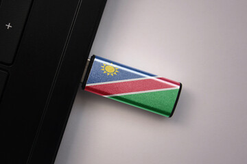 usb flash drive in notebook computer with the national flag of namibia on gray background.