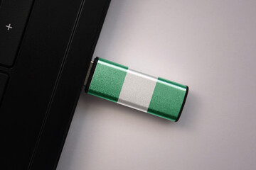 usb flash drive in notebook computer with the national flag of nigeria on gray background.