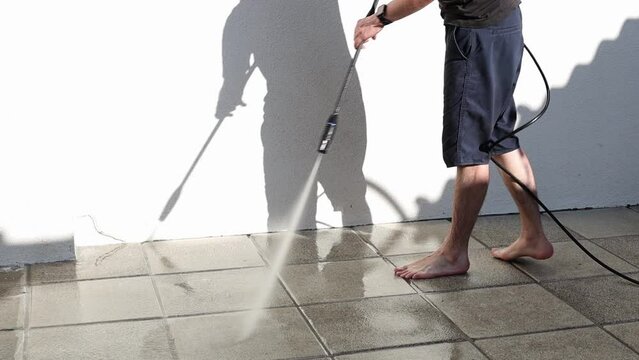 A young man rinses garden tiles in his yard using a Karcher.