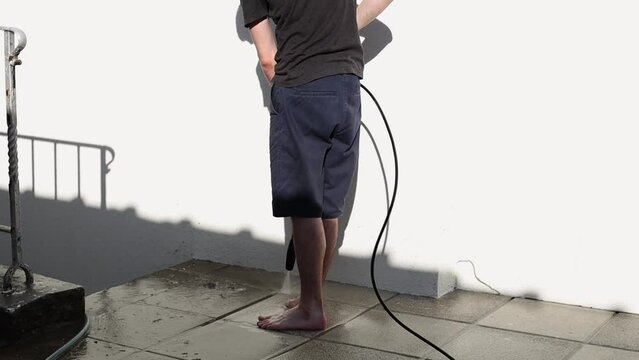 A young man washes garden tiles in his yard using a Karcher.