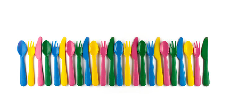 Row of colourful plastic cutlery forks knives spoons isolated on white background. Concept of reusable party and tableware, kids parties lunch dinner, sustainable living, nursery school children food.