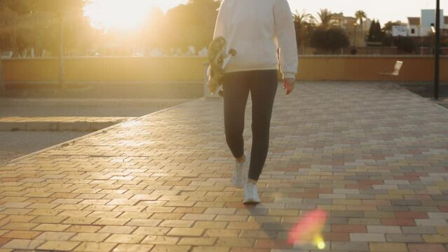 Sporty girl strolls through park, clad in athletic attire, with skateboard in hand, enjoy outdoor ambiance and exercise