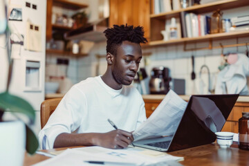 A young businessman working at home with a laptop and papers on his desk, suggesting the flexibility and commitment of remote or home-based work