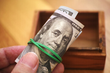 A man holding a one hundred dollar bill above an open wooden box. Close up.