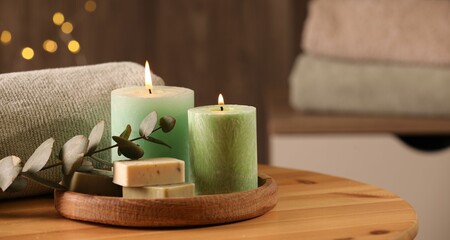 Fototapeta na wymiar Spa composition. Burning candles, soap, towel and eucalyptus branch on wooden table, space for text
