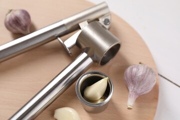 Metal press and garlic on white table, closeup