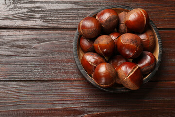 Roasted edible sweet chestnuts on wooden table, top view. Space for text