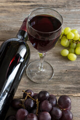 Glass and bottle of red wine and grapes on a old wooden background; vertical picture