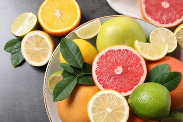 Different fresh citrus fruits and leaves on grey textured table, flat lay