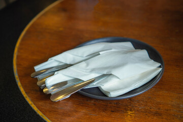Black plate with spoon, fork and tissue on restaurant wooden table