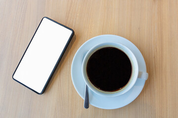 Fototapeta na wymiar smartphone with blank white screen for mock up template background and cup of coffee cup on wooden table
