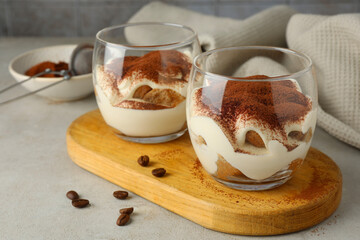 Delicious tiramisu in glasses and scattered coffee beans on light table