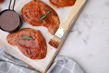 Raw marinated meat, rosemary and basting brush on white marble table, top view. Space for text