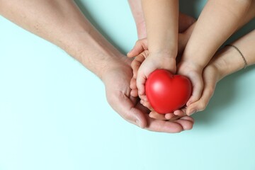 Parents and child holding red decorative heart on light blue background, top view. Space for text