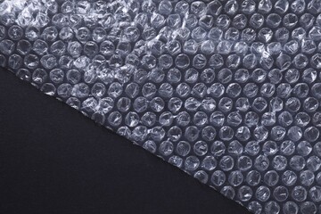 Transparent bubble wrap on black background, top view. Space for text