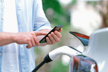 Modern eco-friendly man recharging electric vehicle from EV charging station, using Innovative EV...