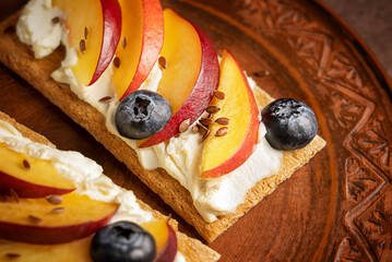 Close up view of sandwich made with crispbread decorated with cream cheese, sliced nectarine, blueberries and seeds served on brown ceramic plate as healthy organic sweet dessert for breakfast