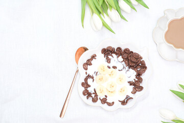The concept of a healthy breakfast of vegetarian yogurt, cornflock and fresh fruit, coffee, flowers white tulips on white background. Top view.