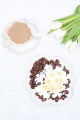 The concept of a healthy breakfast of vegetarian yogurt, cornflock and fresh fruit, coffee, flowers white tulips on white background. Top view.