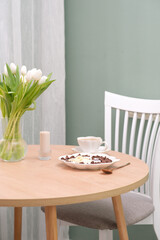 The concept of a healthy breakfast of vegetarian yogurt, cornflock and fresh fruit, coffee, candle, vase with flowers on wooden table on green background. .