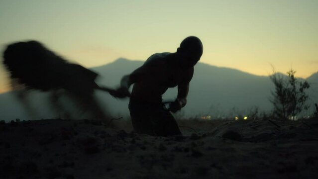 Silhouette of a man with a shovel digging a big hole on the ground.