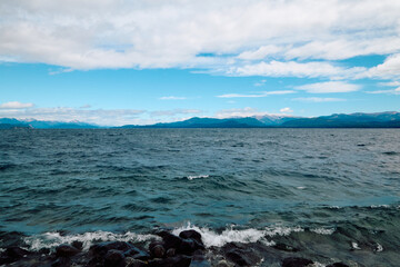 beautiful landscape of a lake against a backdrop of mountains under a clear blue sky, rocky surf