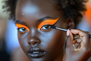 Obraz premium A makeup artist crafts a striking orange eyeshadow look on a model with a radiant complexion.