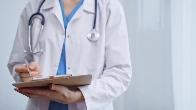 Female doctor taking notes on clipboard. Close-up of a unrecognizable female healthcare professional writing and filling um medication history records form while standing straight in clinic